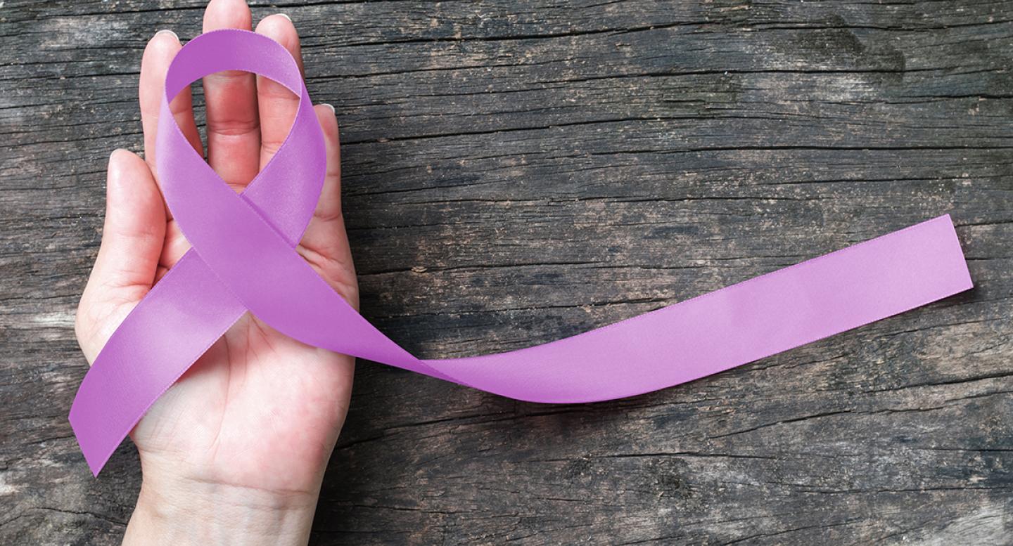 Hand holding a purple ribbon for gynecologic oncology support