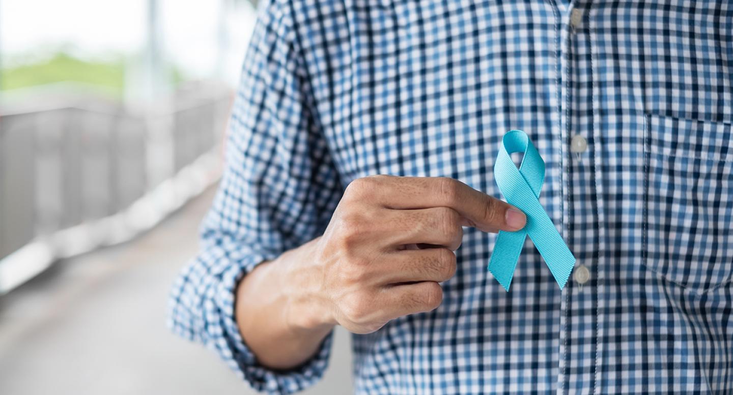 A man in a checked shirt holds an aqua ribbon for prostate cancer awareness