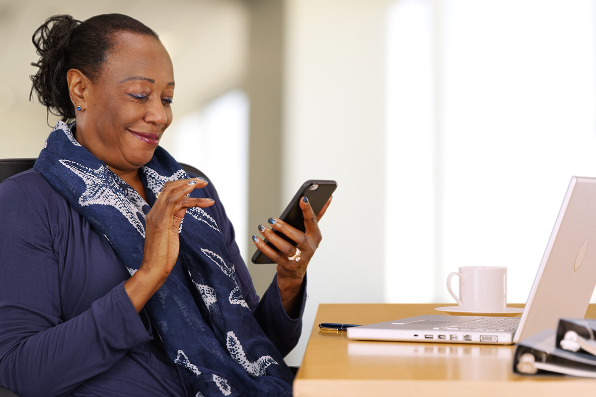 mature woman working on phone and laptop desk