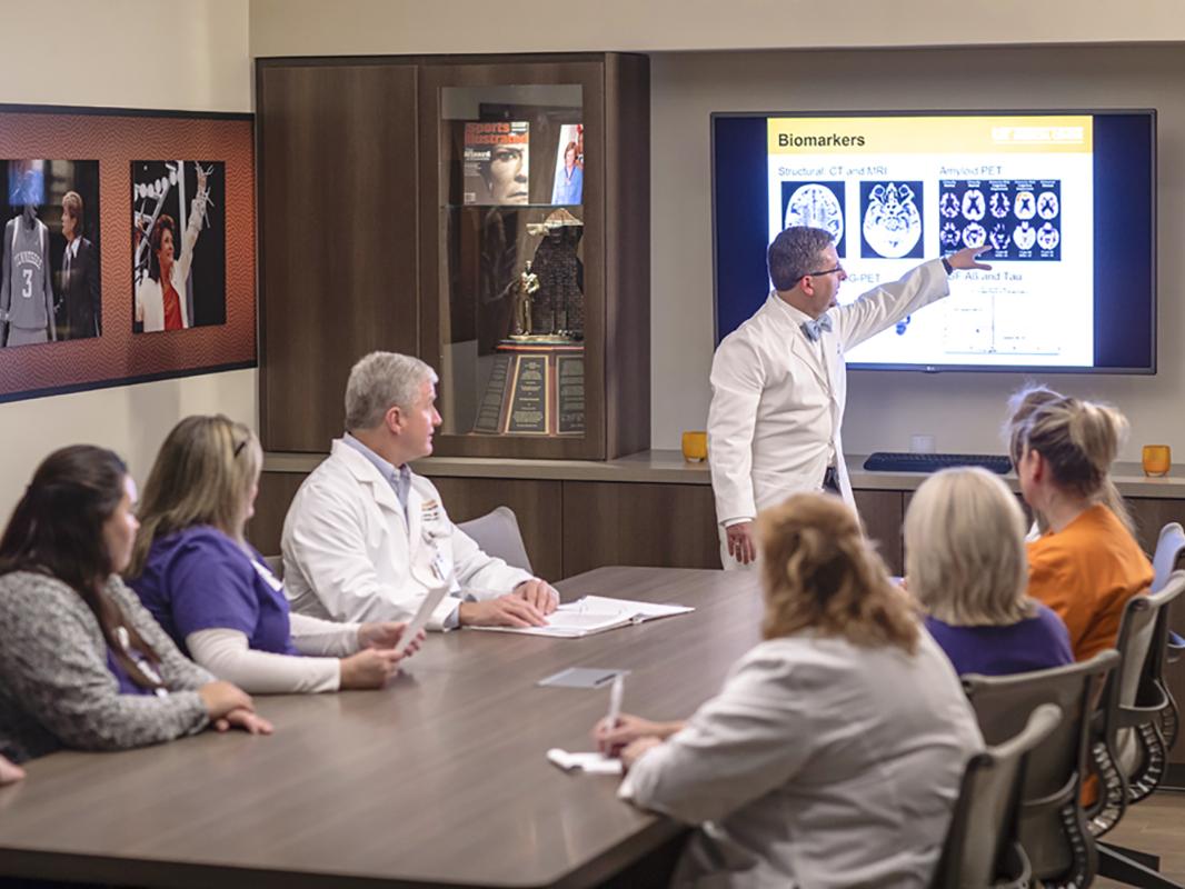 A doctor points at a screen with scans in a conference room