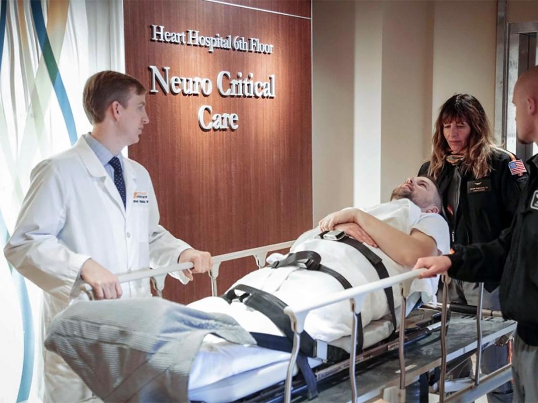 A doctor and EMTs roll a patient into the Neurocritical Care department