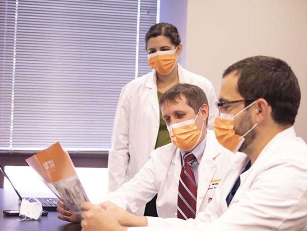Three doctors wearing masks read a brochure about Deep Brain Stimulation