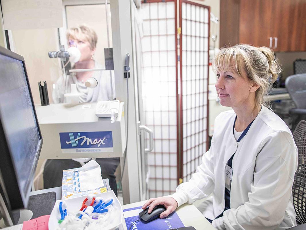 A technician reads a computer screen as a patient breathes into a spirometer