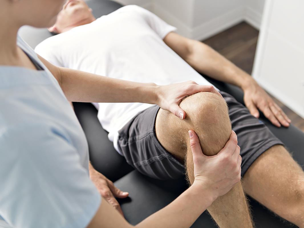 A man on a therapy table receives physical therapy on his knee