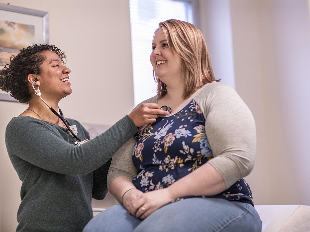 A midwife listens to a patient's heartbeat in an exam room