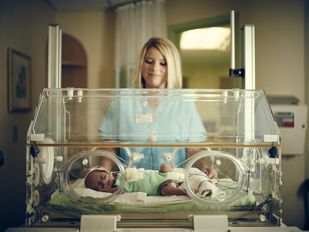 A NICU nurse comforts a premature baby in an incubator