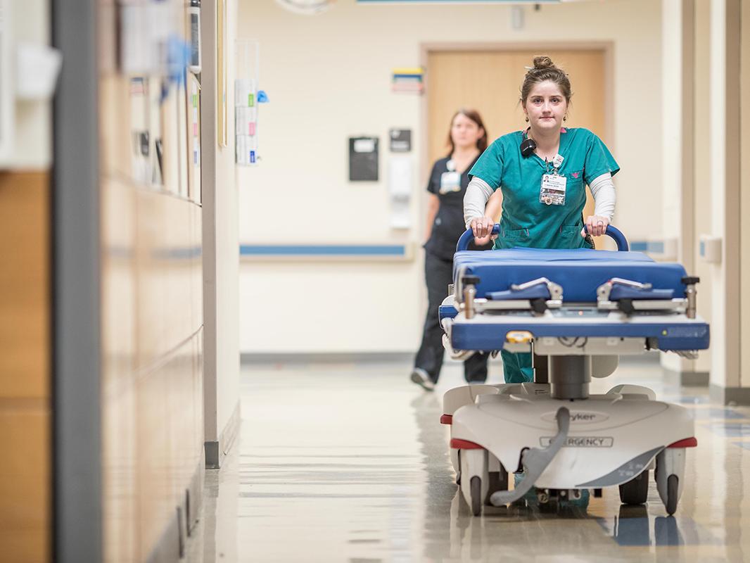 A nursing technician pushes a stretcher down a hospital hallway