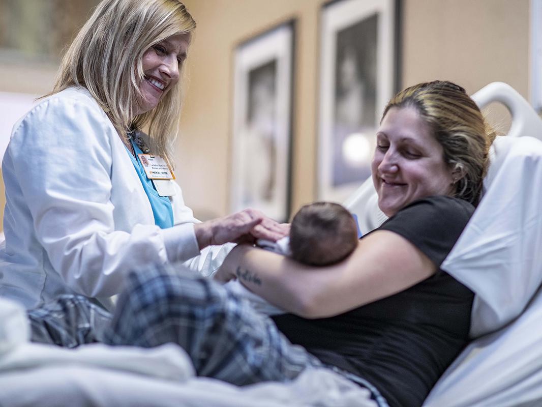 A mom holds a newborn baby in the hospital while a nurse looks on