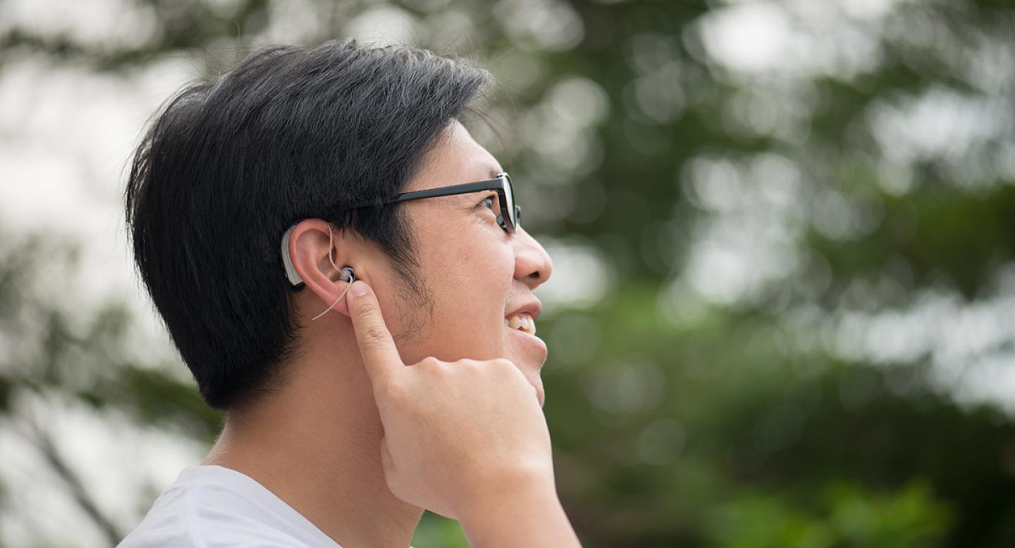 A man points at a hearing aid in his ear