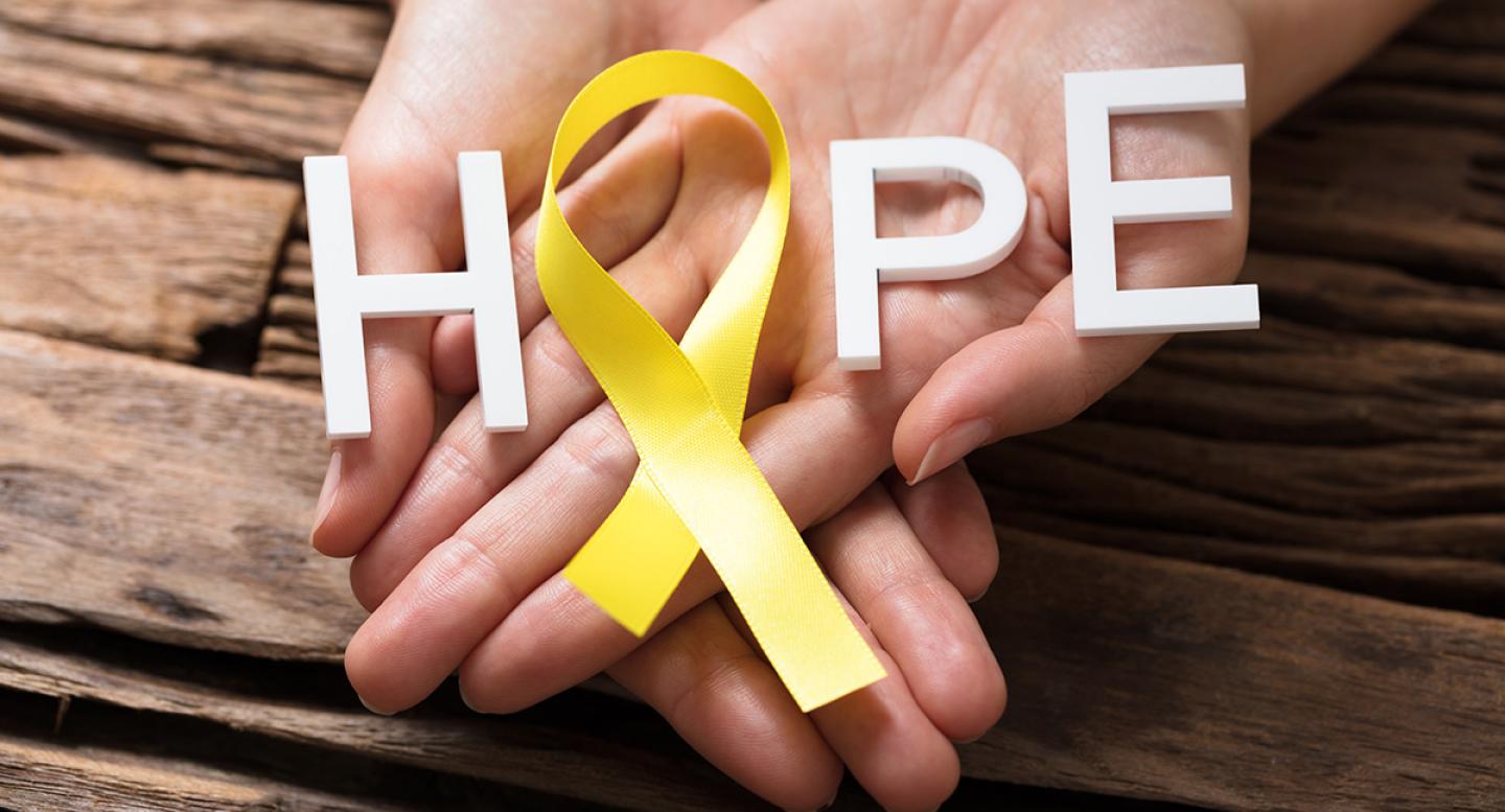 Hands hold a yellow ribbon making an O in the middle of the world HOPE for bladder cancer awareness