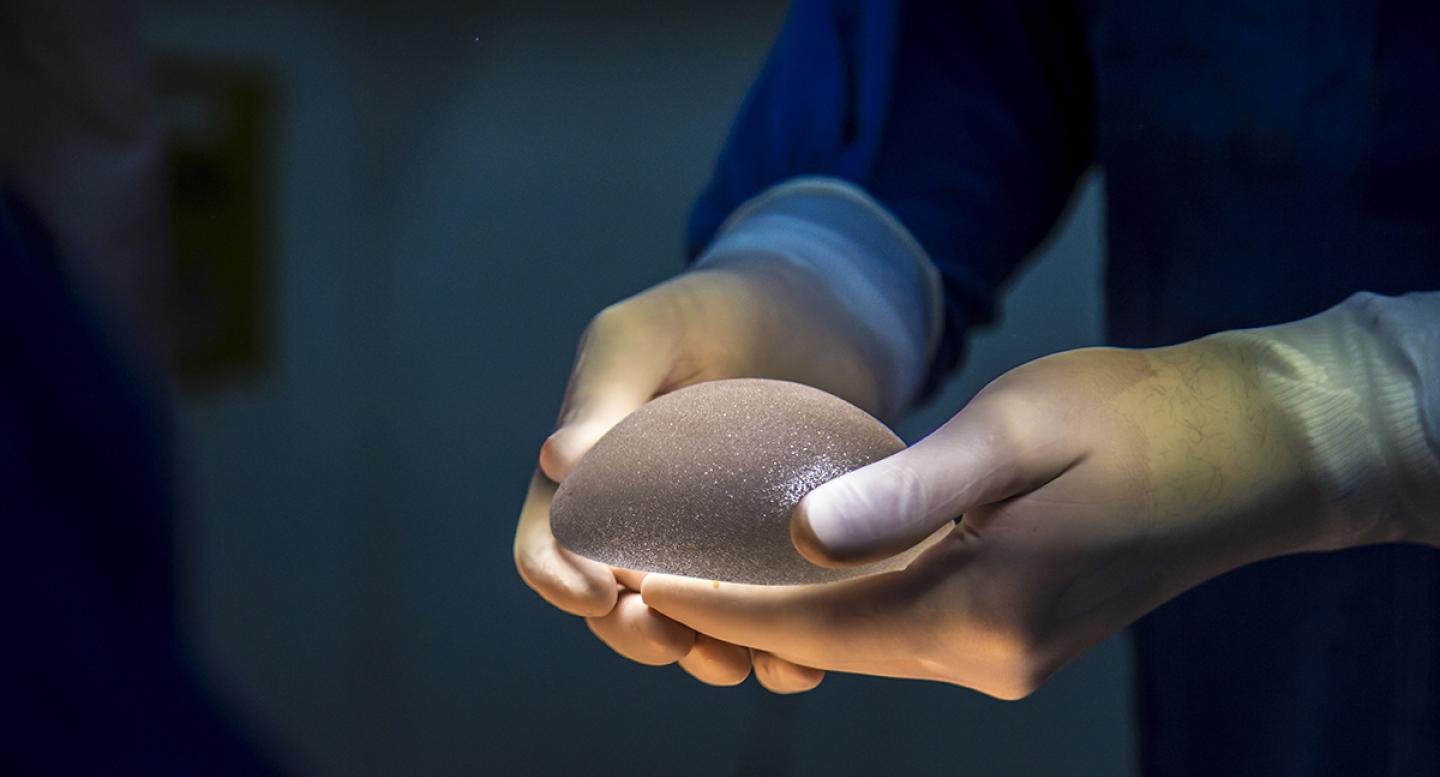 A doctor holds a breast implant in gloved hands
