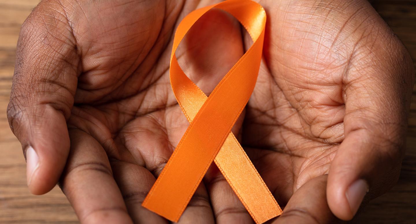 A black man's hands hold an orange ribbon for kidney cancer