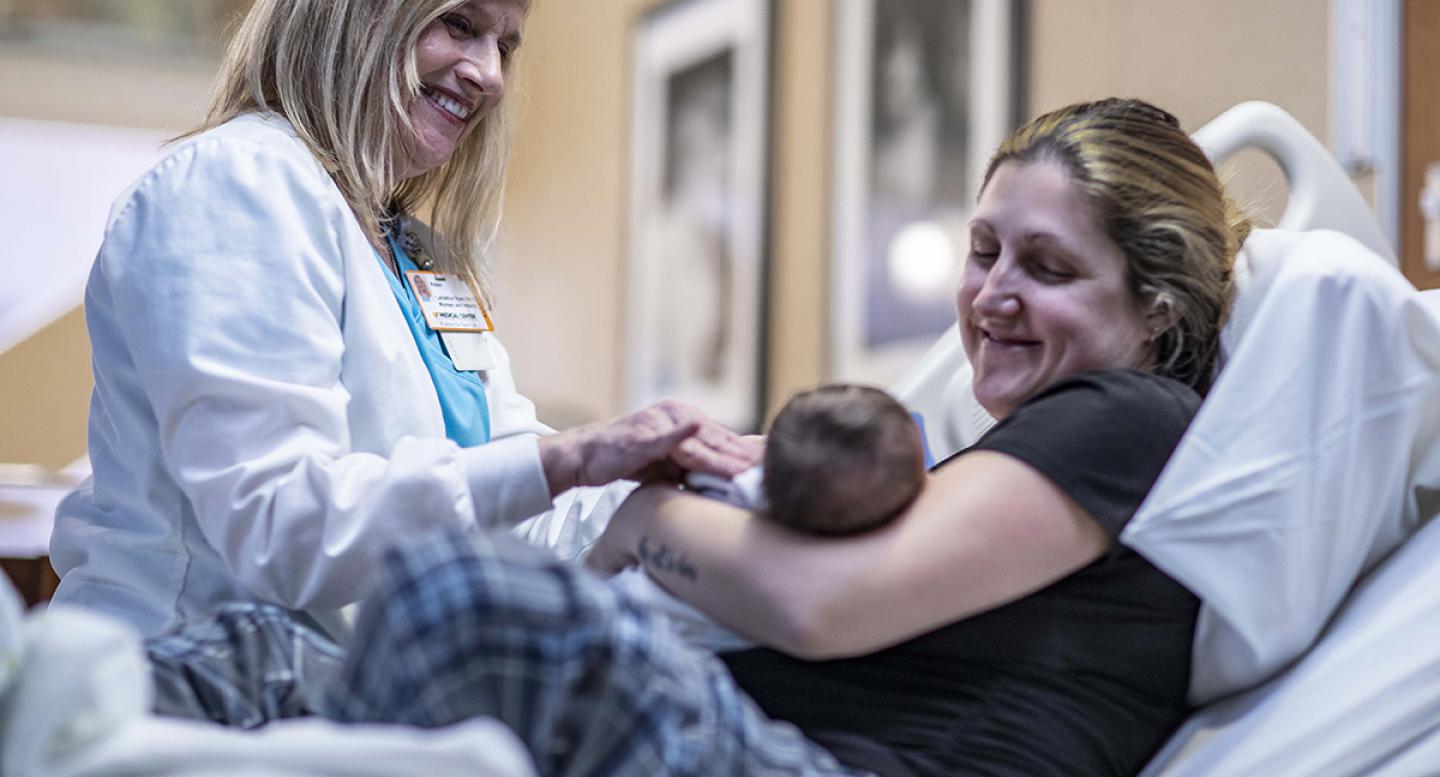 A mom holds a newborn baby in the hospital while a nurse looks on