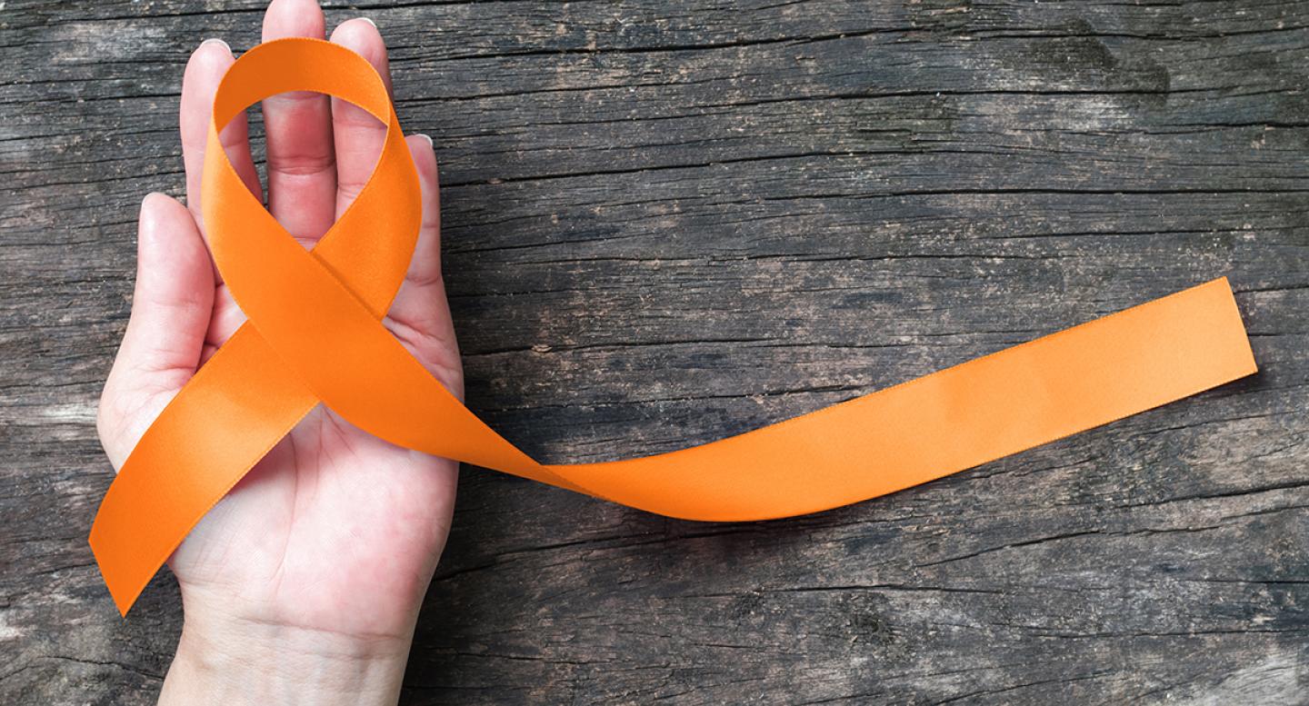 A woman's hand holds an orange ribbon for leukemia