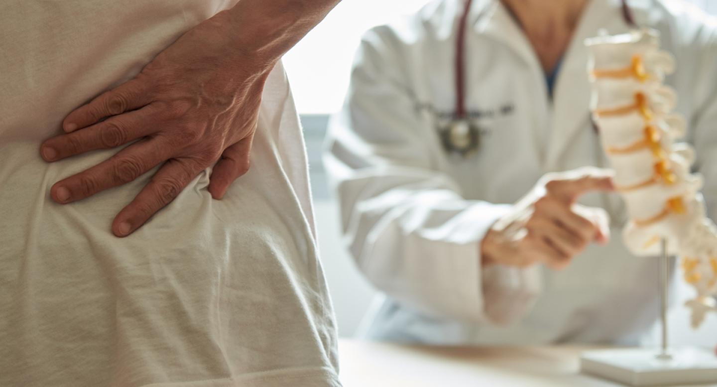 A patient with back pain talks with a doctor with a model of the spine