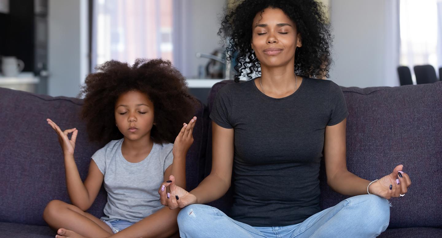 Mother and daughter meditating with crossed legs and touching fingertips