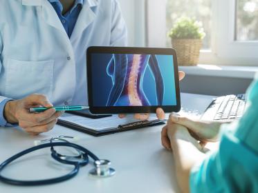 A doctor points at an image of a spine with osteoporosis on a tablet