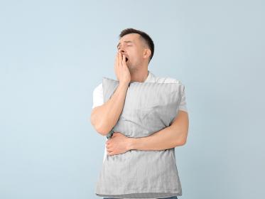 A man yawns while he holds a pillow