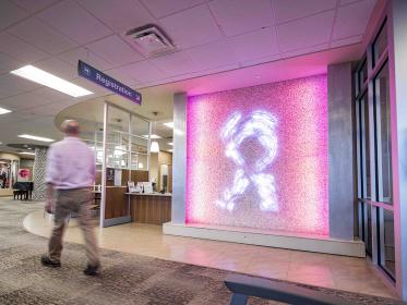 A man walks through the University Breast Center, passing in front of a lighted pink ribbon sign