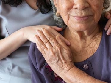 A senior palliative care patient holds hands with her nurse