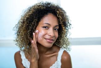 A Black woman applies moisturizer to her face
