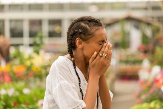 A Black woman in the park sneezes with outdoor allergies