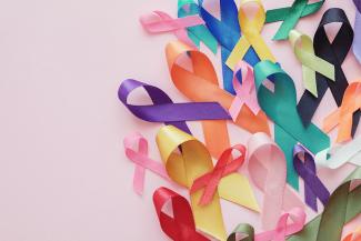 A variety of different colored cancer awareness ribbons on a pink background