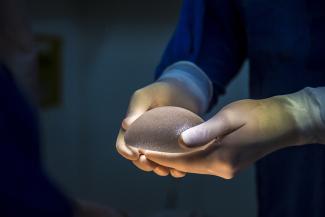 A doctor holds a breast implant in gloved hands