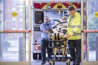 EMTs roll a patient on a stretcher from an ambulance to the Emergency Department