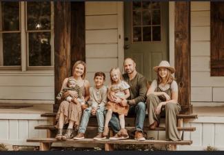 A mother, father and four kids sit on a porch