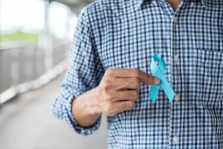 A man in a checked shirt holds an aqua ribbon for prostate cancer awareness