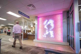 A man walks through the University Breast Center, passing in front of a lighted pink ribbon sign