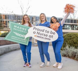 Three nurses holding a sign in front of a hospital