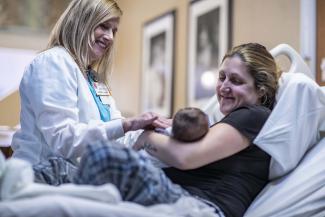 A mom holds a newborn baby in the hospital while a nurse looks on