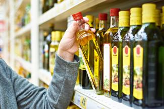 A woman takes a bottle of olive oil off a grocery store shelf