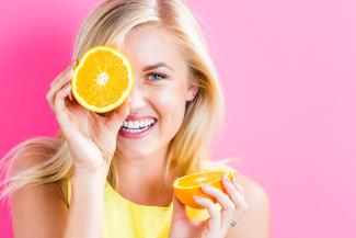 A woman dressed in yellow holds half an orange up to her eye