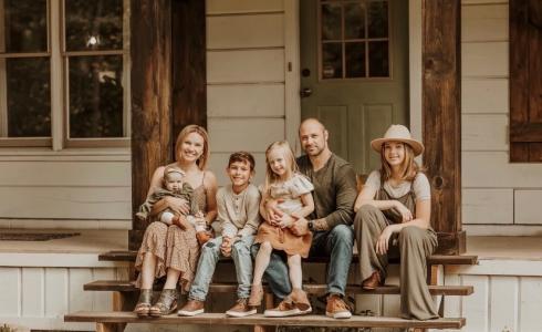 A mother, father and four kids sit on a porch