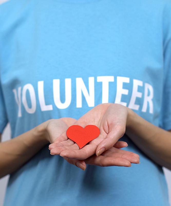A person wearing a blue t-shirt with "volunteer" on the front, holding a red heart