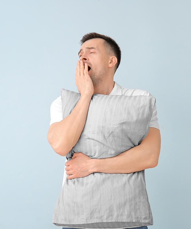 A man yawns while he holds a pillow