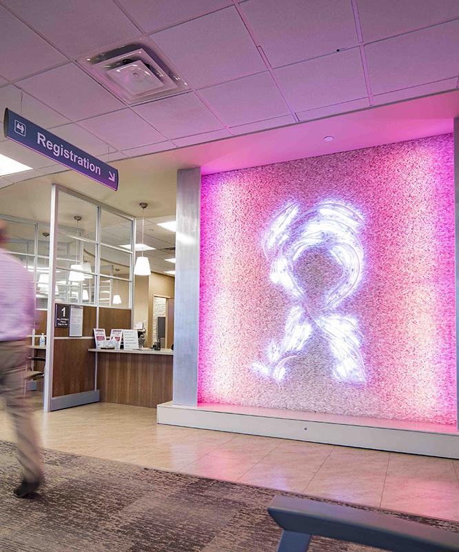 A man walks through the University Breast Center, passing in front of a lighted pink ribbon sign