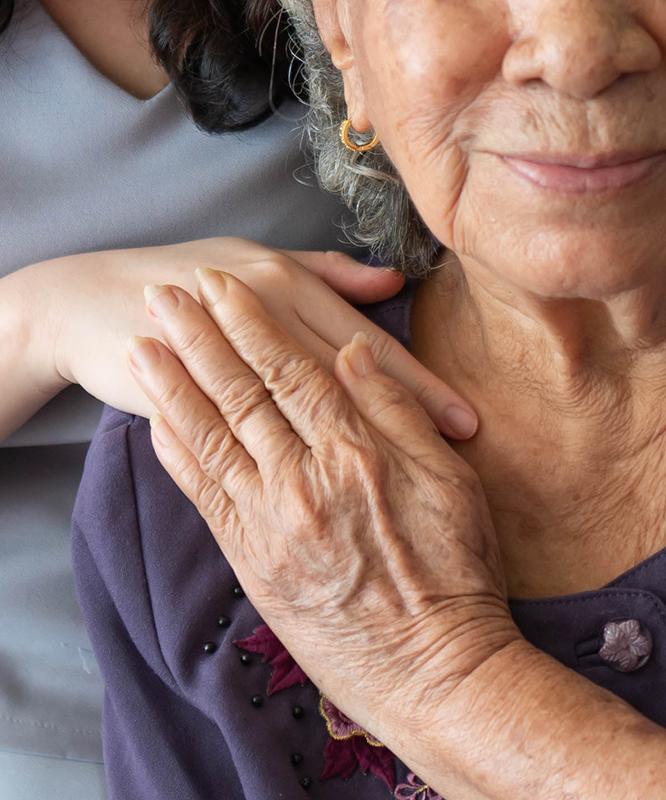 A senior palliative care patient holds hands with her nurse